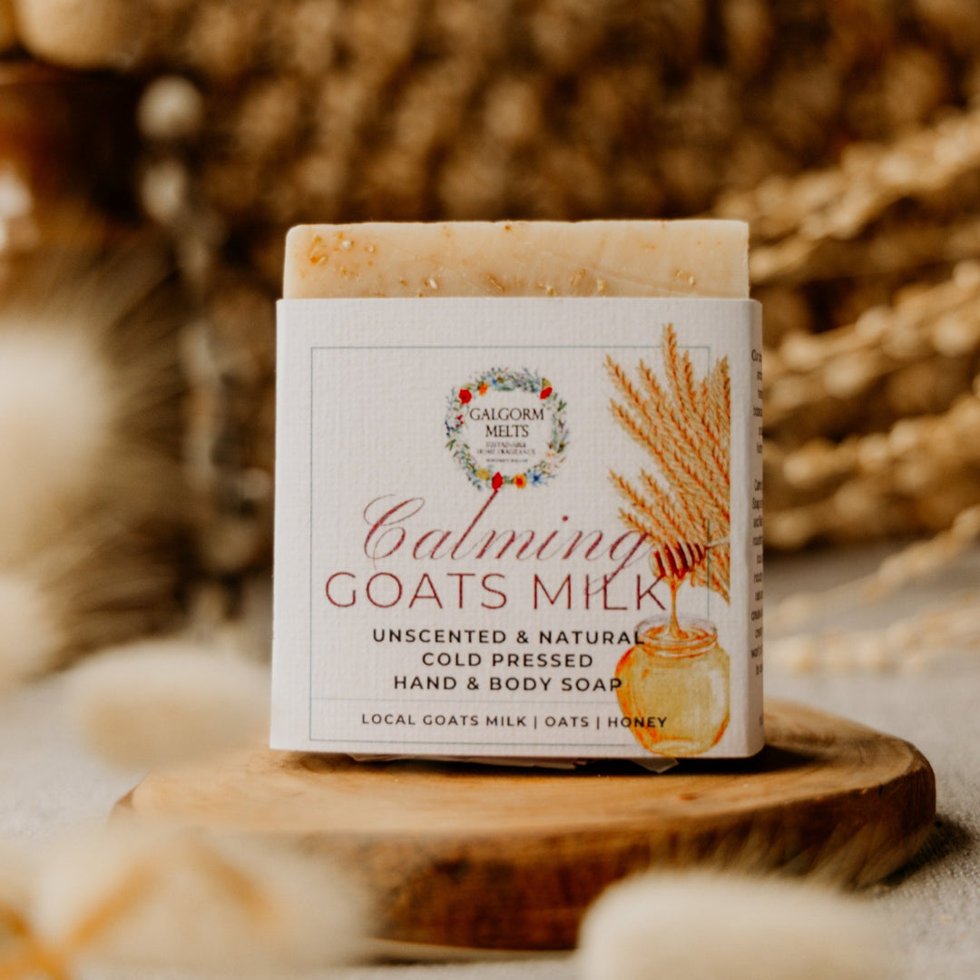 Bar of CALMING GOATS MILK soap with a label on a wooden stand against a blurred natural background