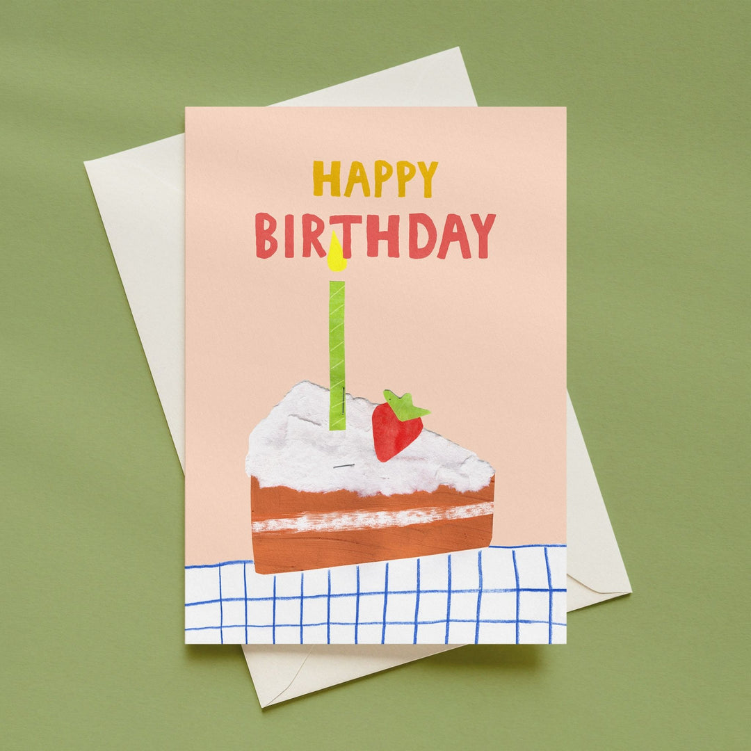 A square birthday card with a peach background, featuring a hand-drawn slice of cake with white frosting, a red strawberry, and a single green candle. The text 'HAPPY BIRTHDAY' is printed on the card, with 'HAPPY' in yellow and 'BIRTHDAY' in red.
